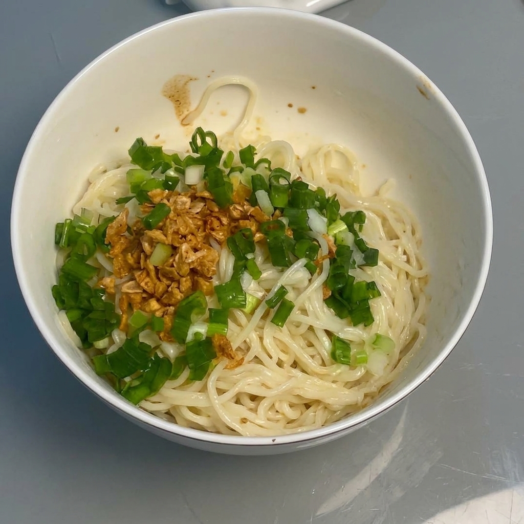 Noodles being mixed with sauce, garlic, and onions using chopsticks.