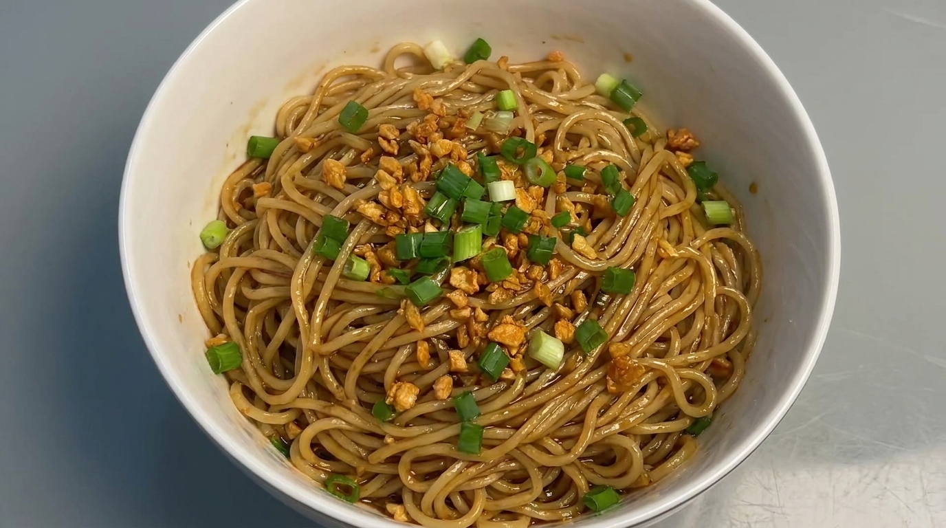 A bowl of garlic oil tossed noodles, featuring a glossy soy-based sauce and topped with crunchy fried garlic and fresh green onions.