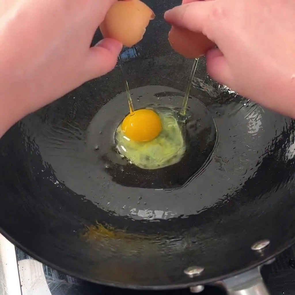 Two fresh eggs cracking and sizzling in a hot, oiled wok to achieve crispy edges.