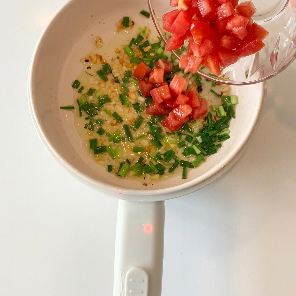 Diced red tomatoes added to the pot containing sautéed garlic and green onions.
