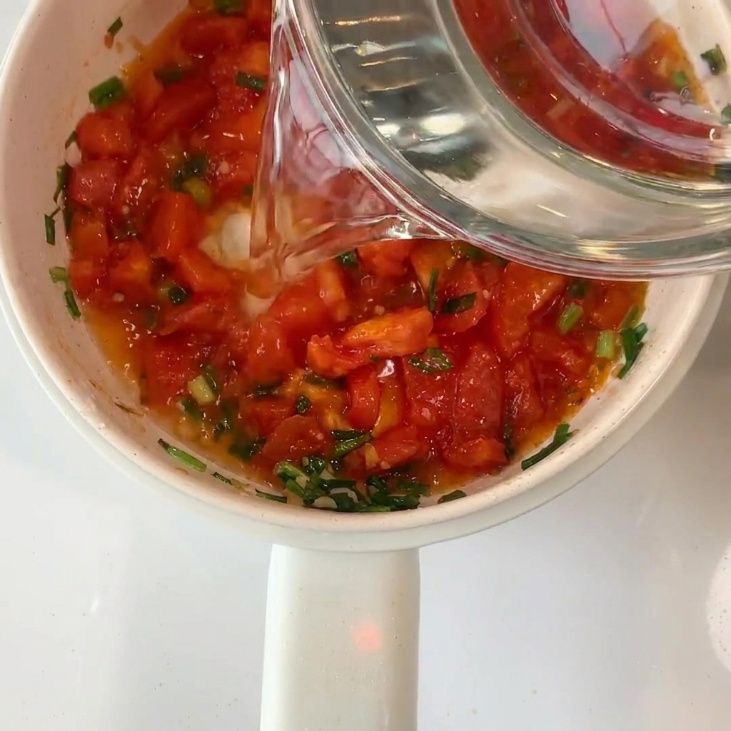 Clear water being poured from a glass bowl into the pot with tomatoes.