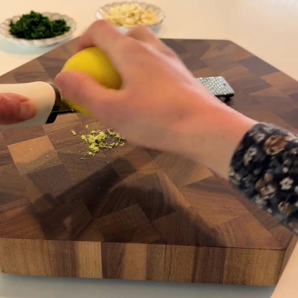 A lemon being zested with a fine grater, showing the yellow zest piling up.