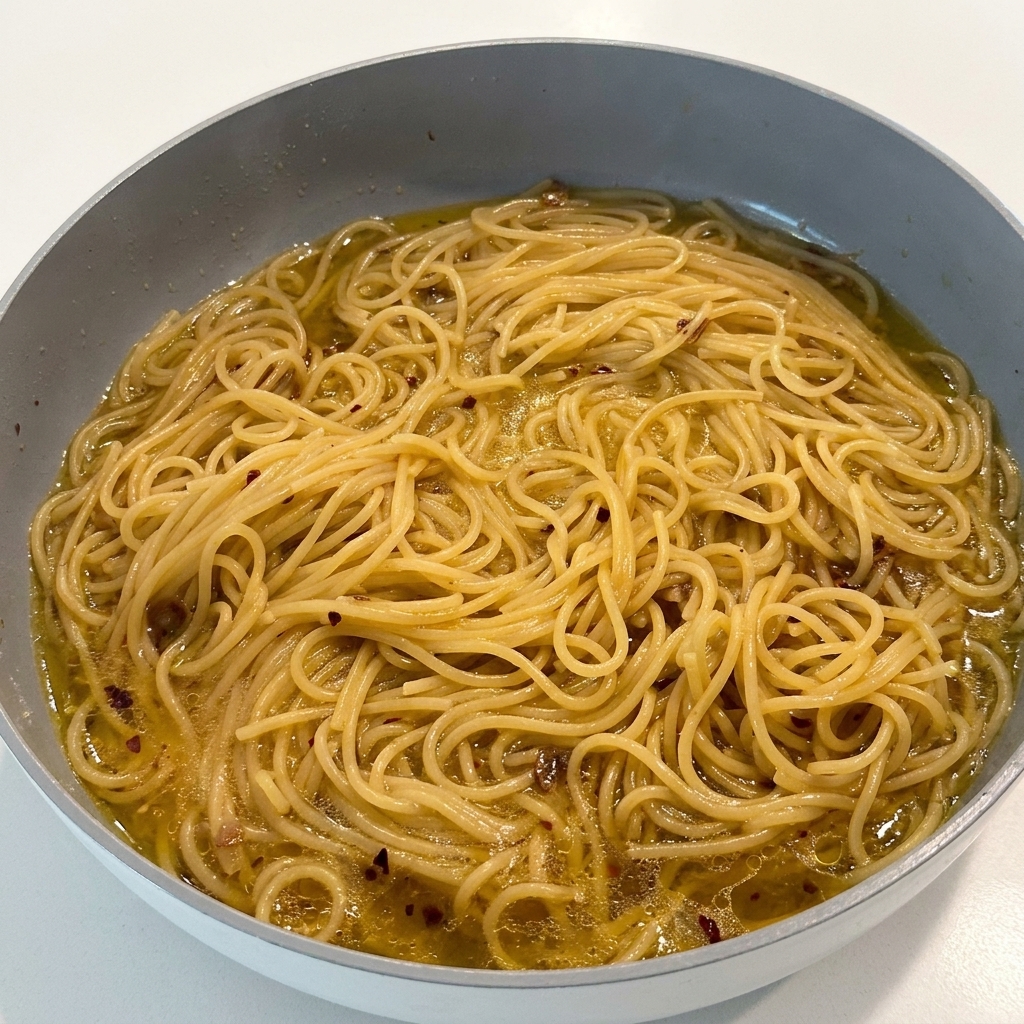 Seasoning the pasta with black pepper while it sits in the skillet.