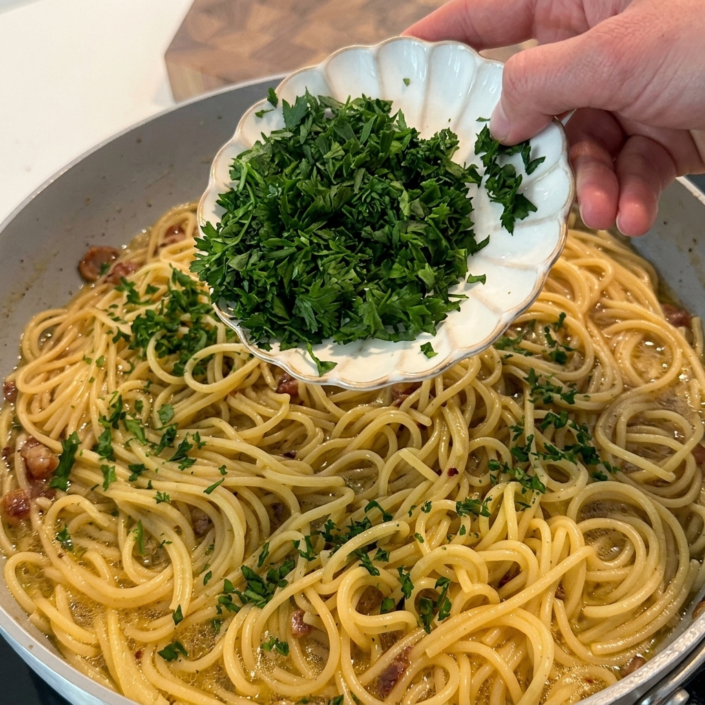 Chopped fresh parsley being sprinkled over the finished pasta in the skillet.