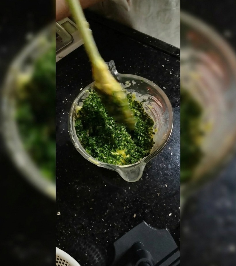 A silicone spatula folding herbs into soft butter inside a glass bowl.