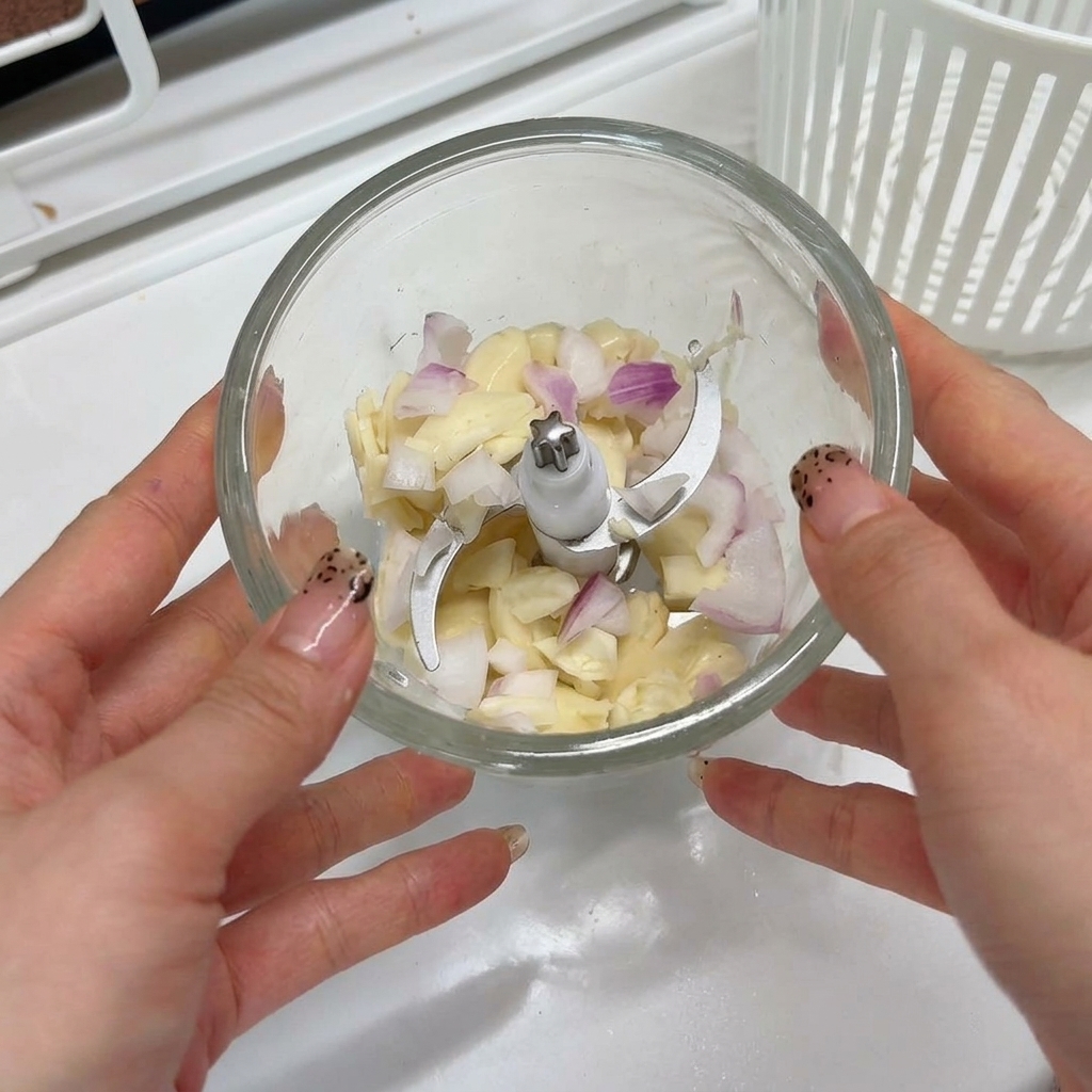 Garlic cloves and chopped shallots sitting inside the bowl of a small food processor ready to be blended.
