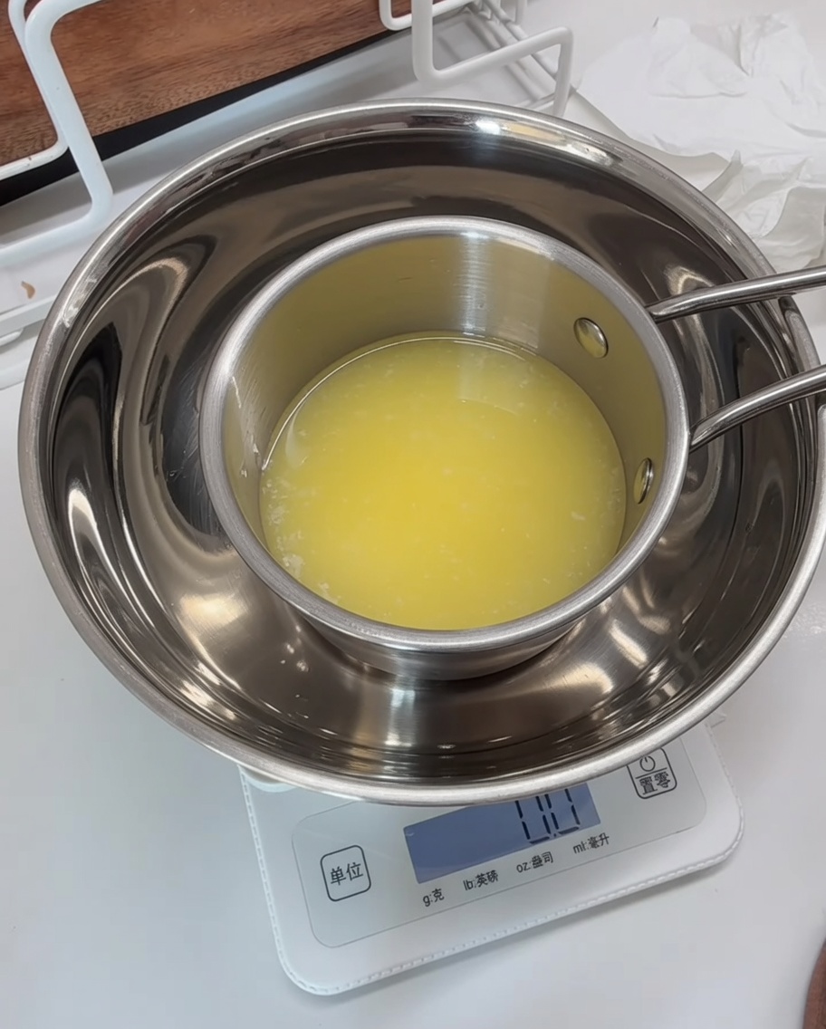 A metal measuring bowl on a digital scale with the parsley mixture being combined with melted butter.