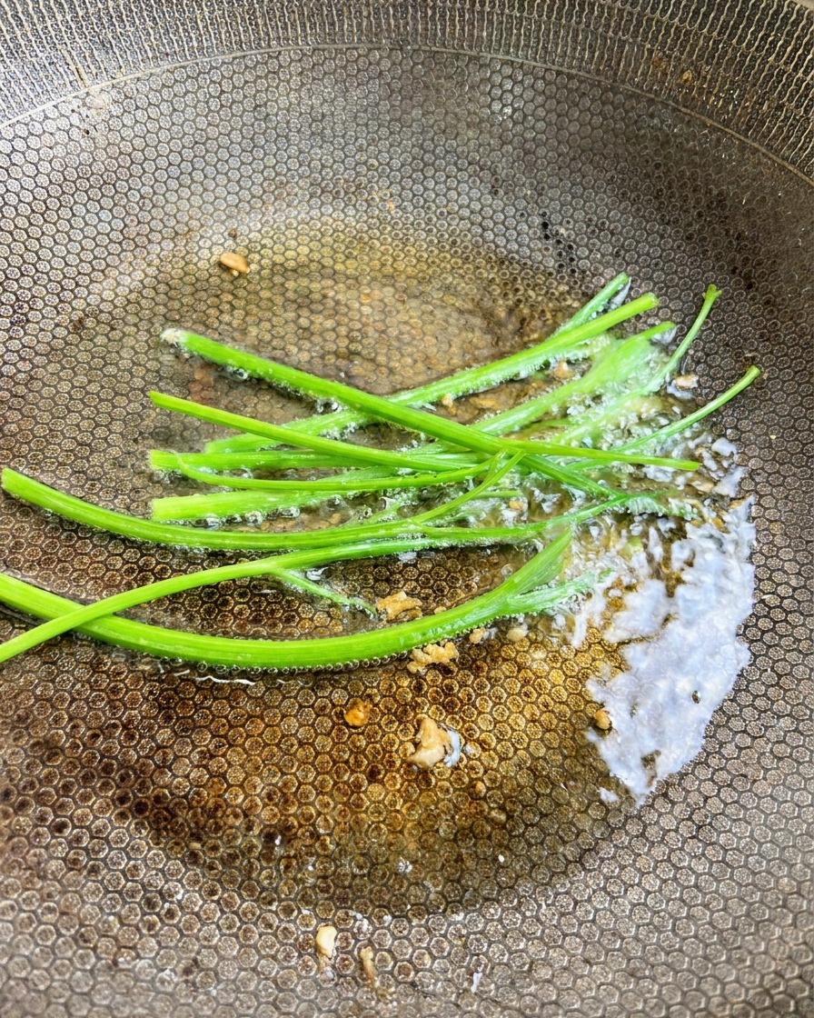 Fresh green parsley stems being added to the garlic-infused oil in the wok.