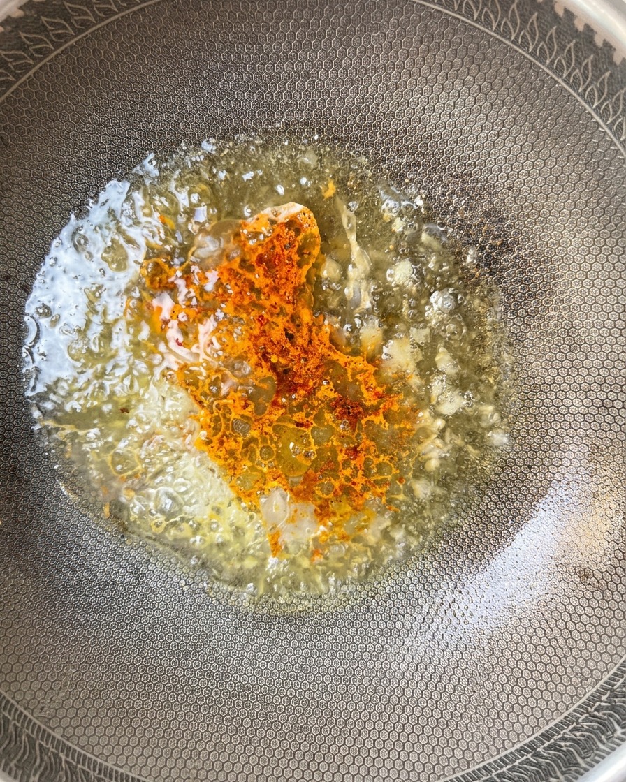 Chili powder being dusted into the bubbling sauce in the wok.