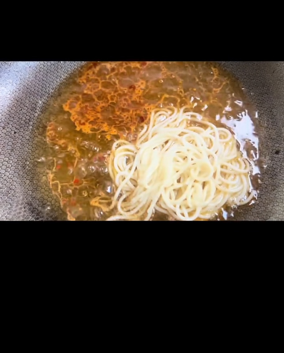 Boiled spaghetti being transferred into the wok to mix with the sauce.