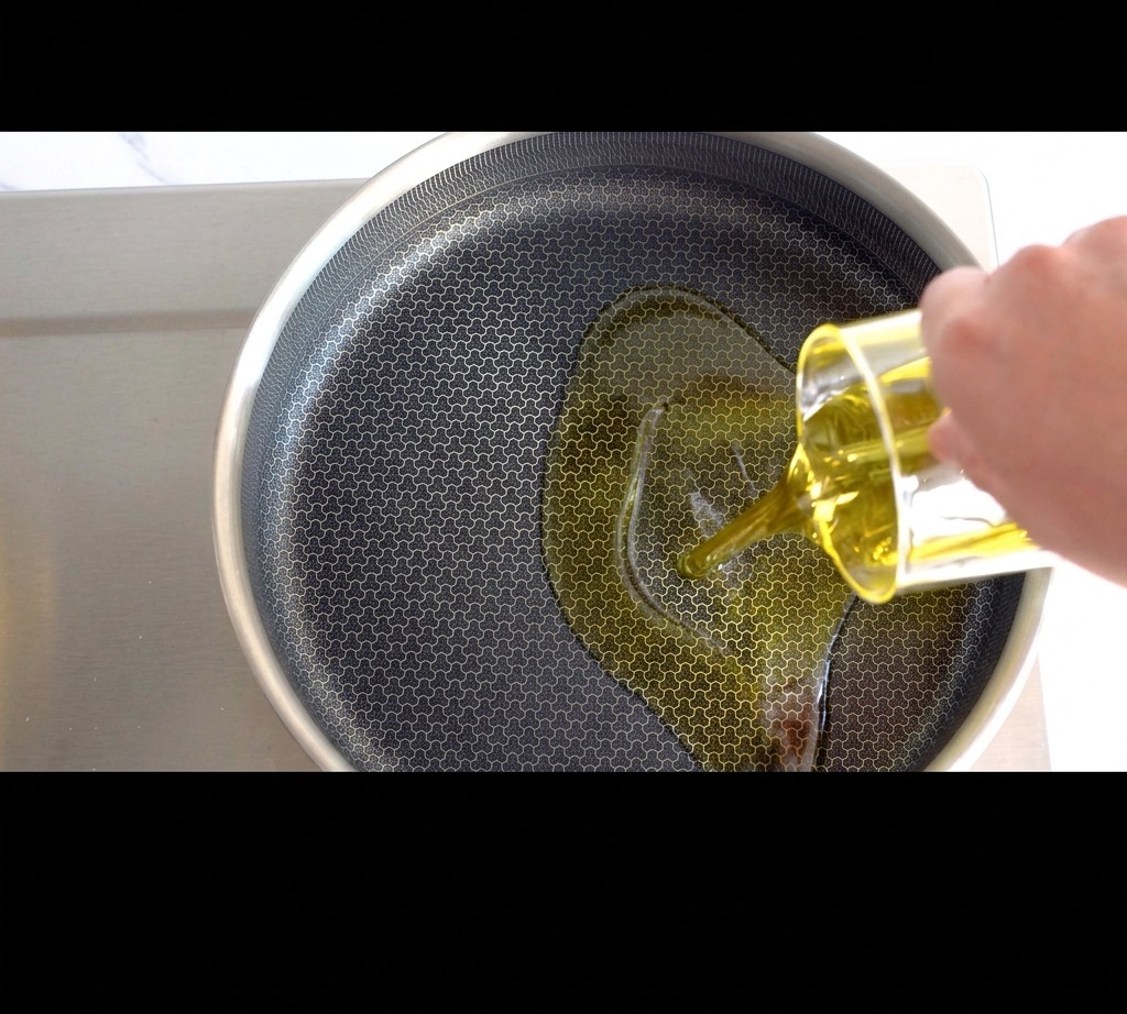Golden olive oil being poured into a frying pan on the stove.