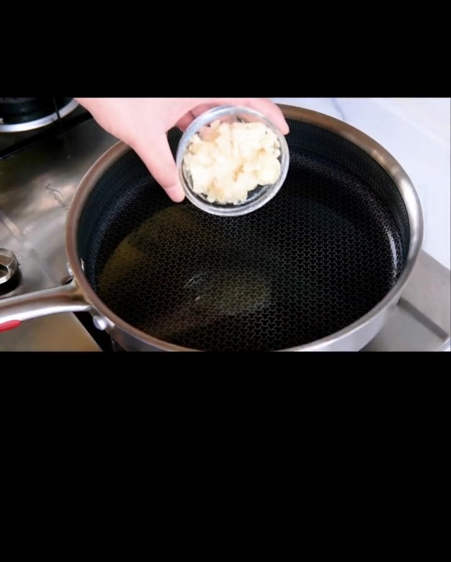 Sliced garlic frying in shimmering olive oil in a pan.