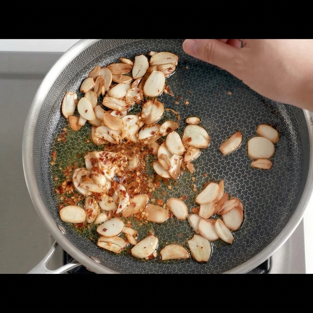 Dried chili pepper pieces being added to the pan with golden fried garlic.