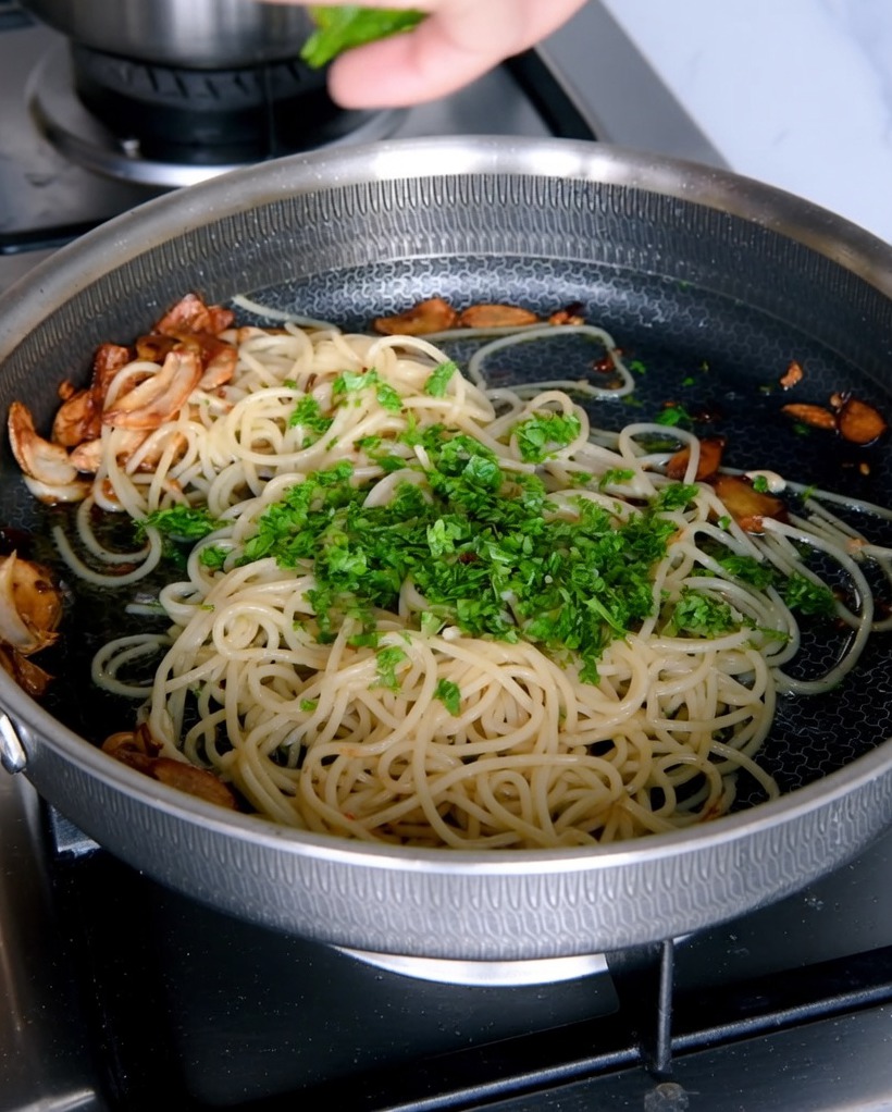 Chopped fresh parsley being added to the pan of garlic spaghetti.