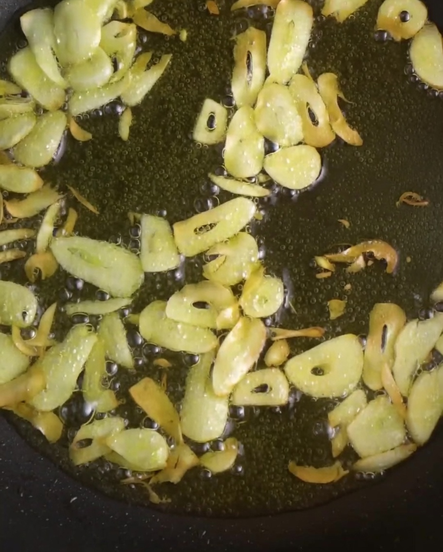 Thinly sliced garlic and vibrant red chili peppers frying in shimmering oil in a pan.