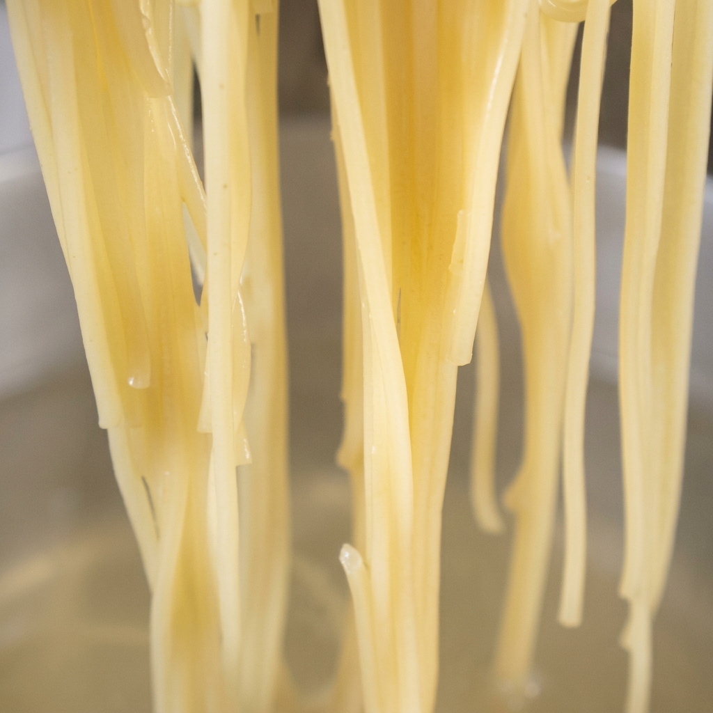 Cooked spaghetti noodles being added to a pan with golden garlic and red chili oil.