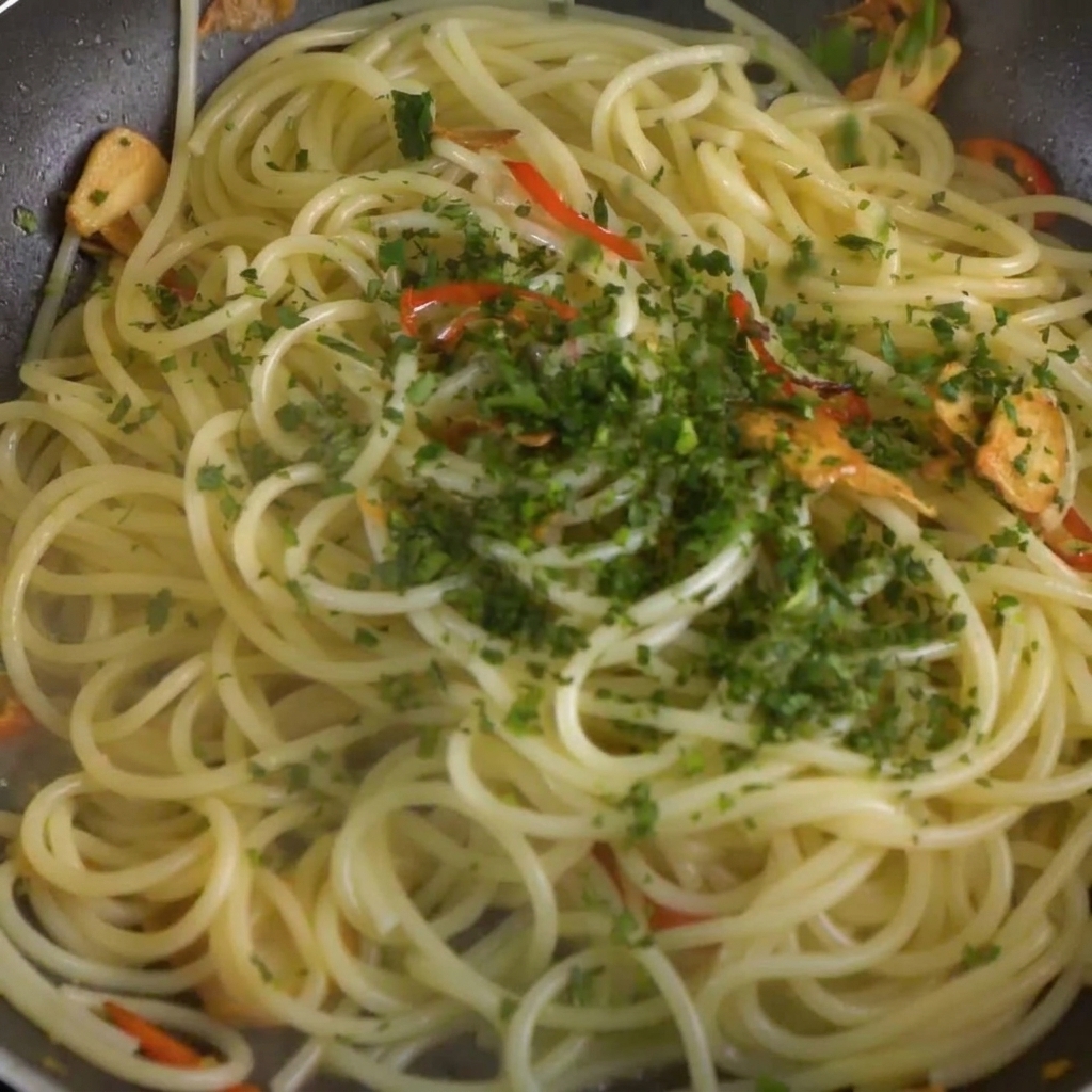 Chopped fresh parsley being scattered over the spaghetti and chili-garlic mixture in the pan.