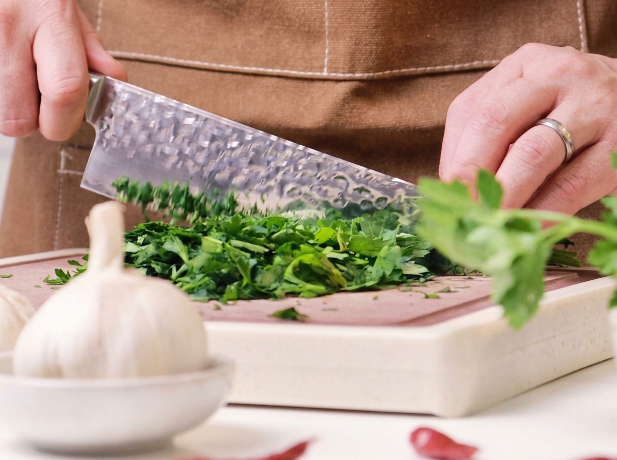 Fresh green parsley being finely minced on a wooden cutting board with a large chefs knife.