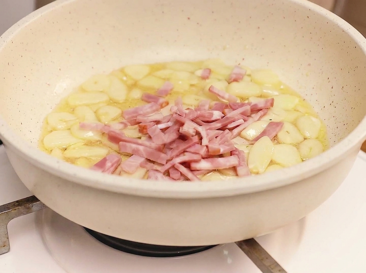 Bacon strips frying in a pan with garlic, reaching a golden-brown, crispy state.