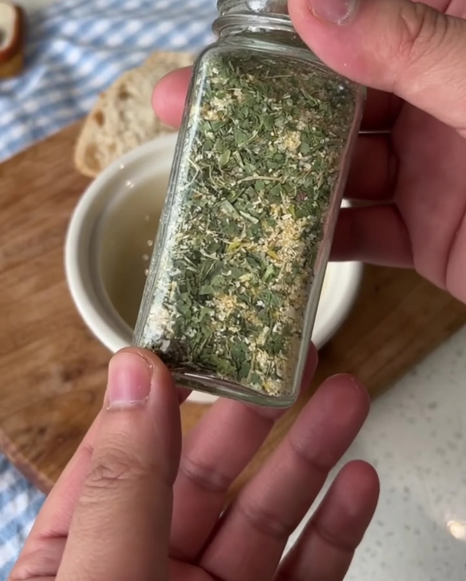 A small ceramic bowl with softened butter, being seasoned with green parsley garlic salt.
