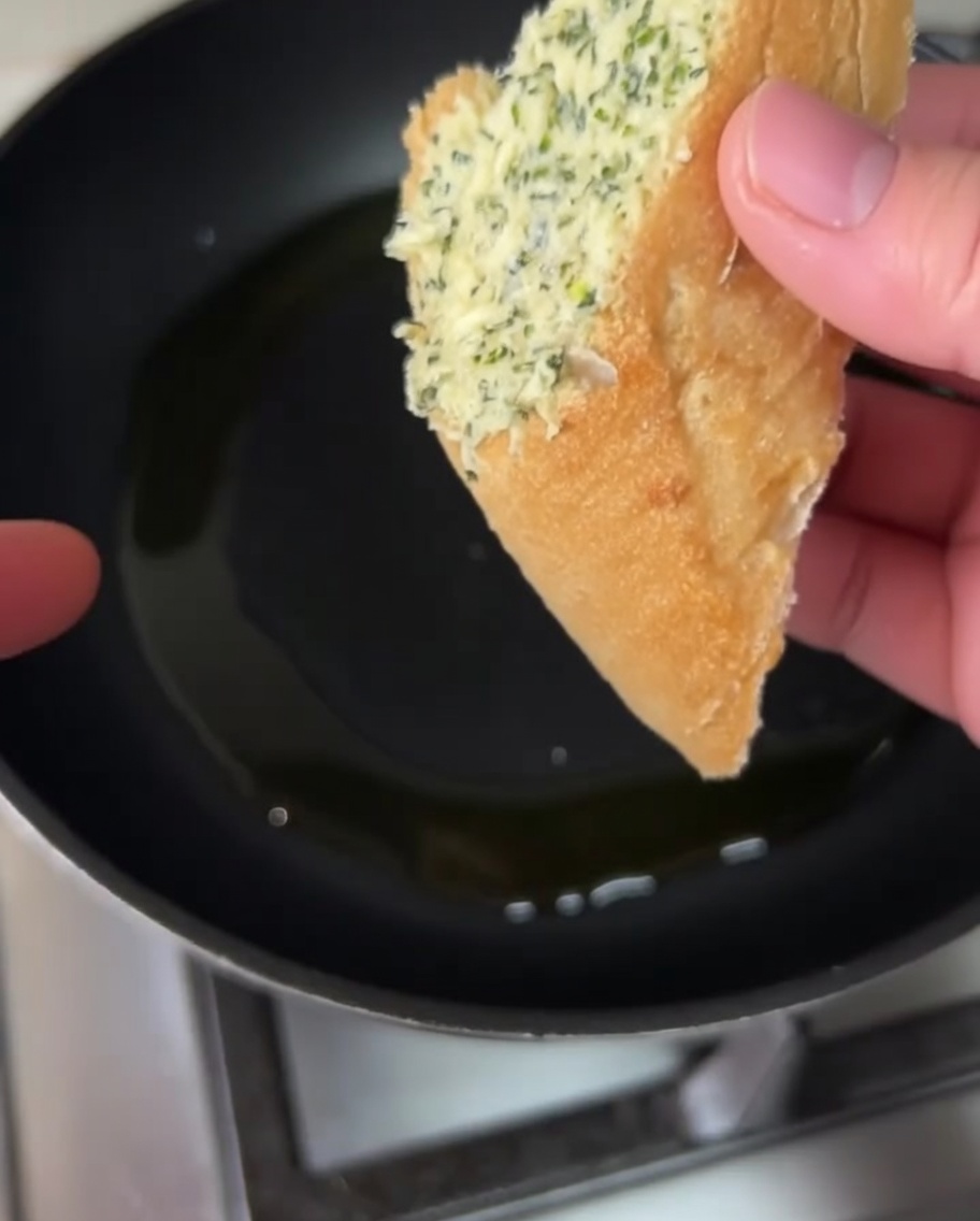 Garlic butter coated bread slices frying in a pan with olive oil.
