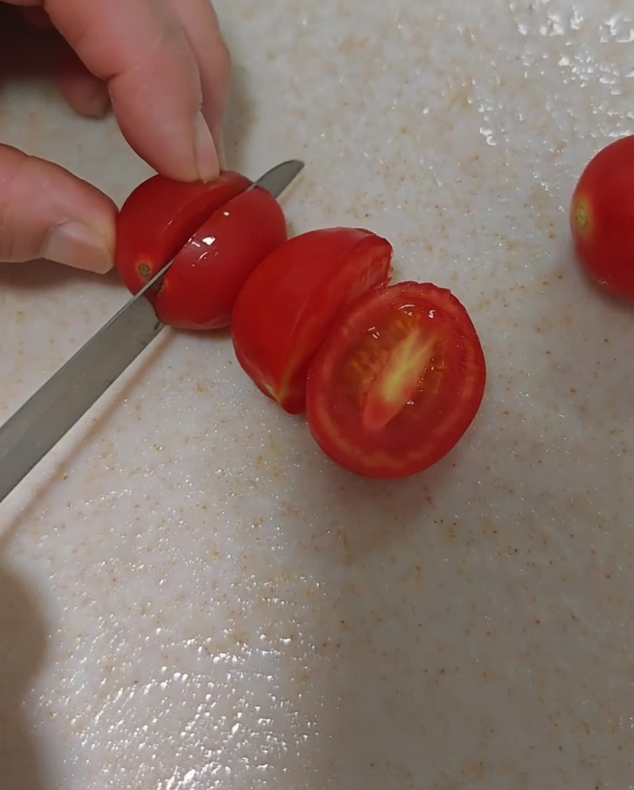 Fresh cherry tomatoes being carefully sliced in half.