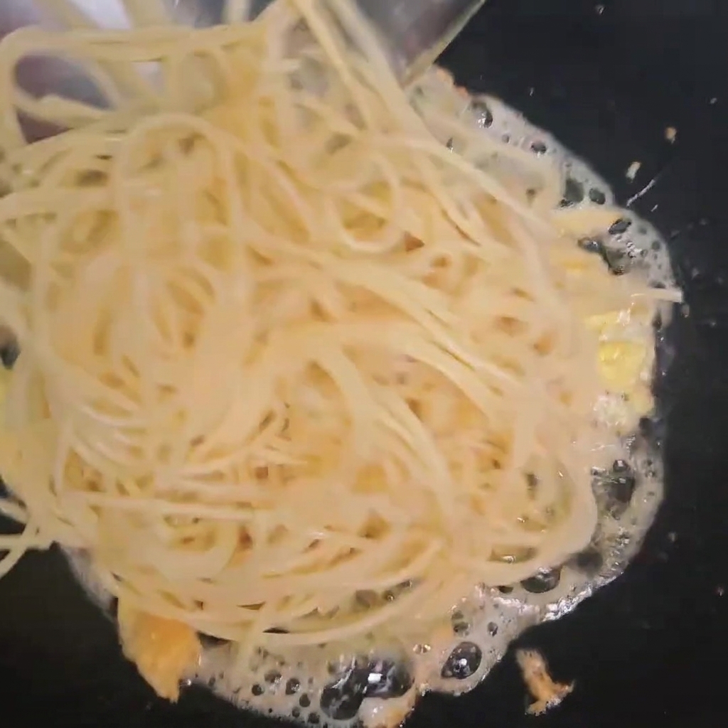 Cooked spaghetti being added into a wok containing fried eggs.