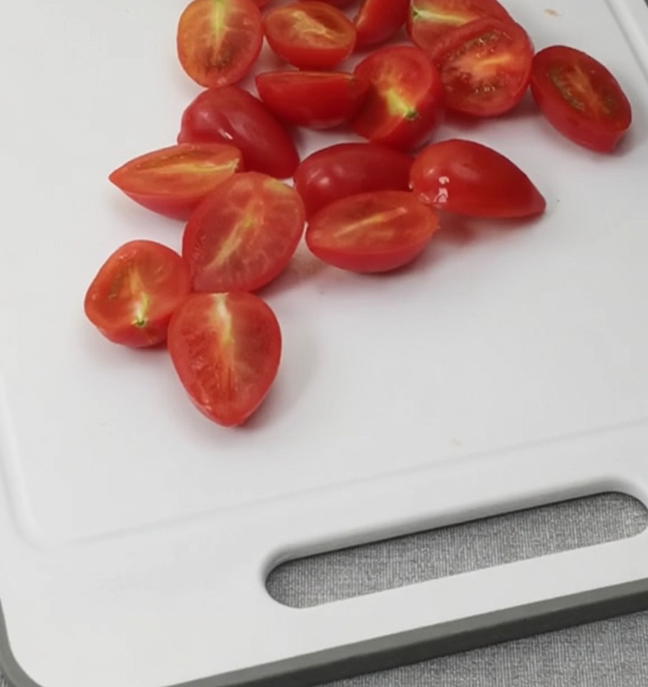 Halved cherry tomatoes resting on a white cutting board.