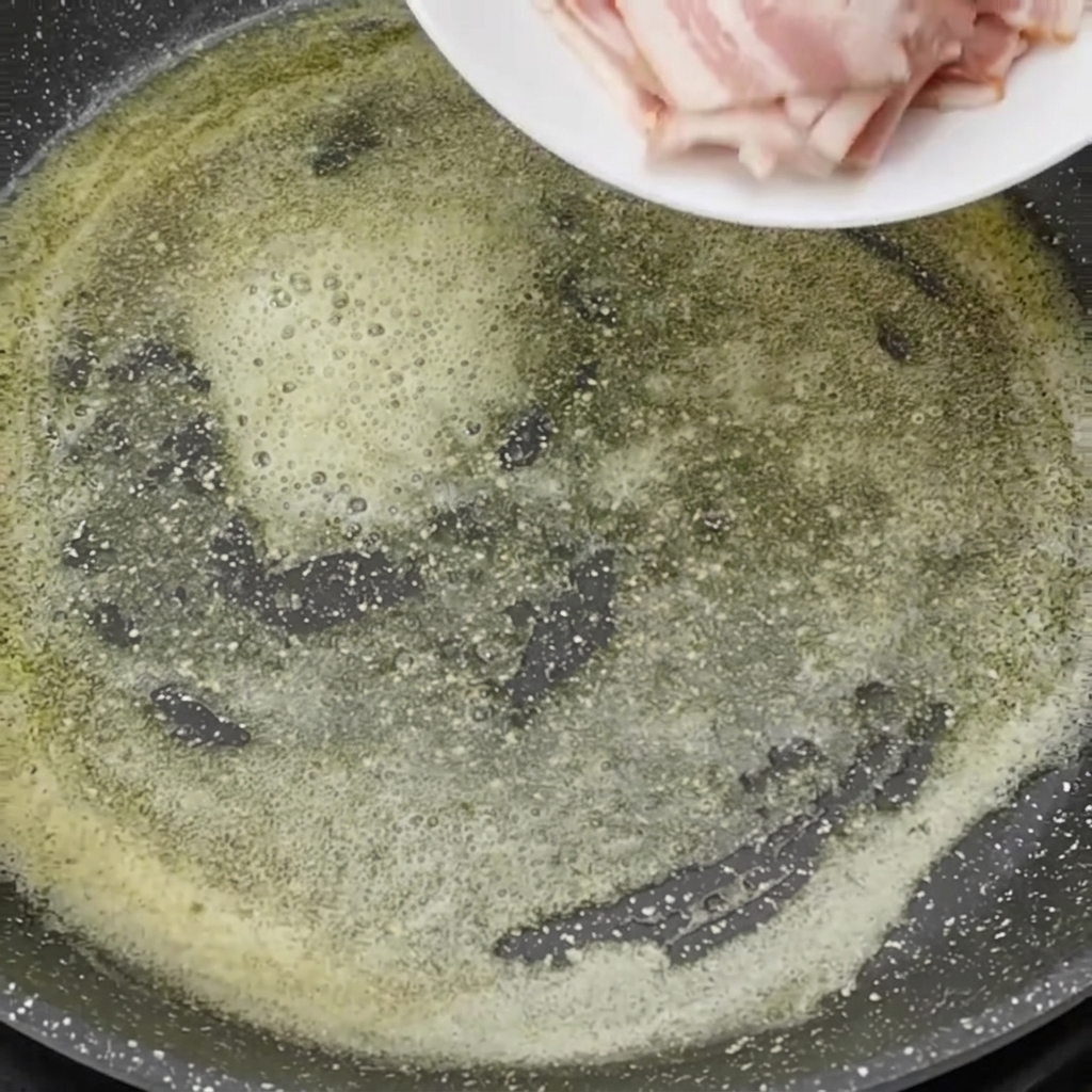 Pieces of raw sliced bacon being pushed off a white plate into a pan with hot, bubbly melted butter.