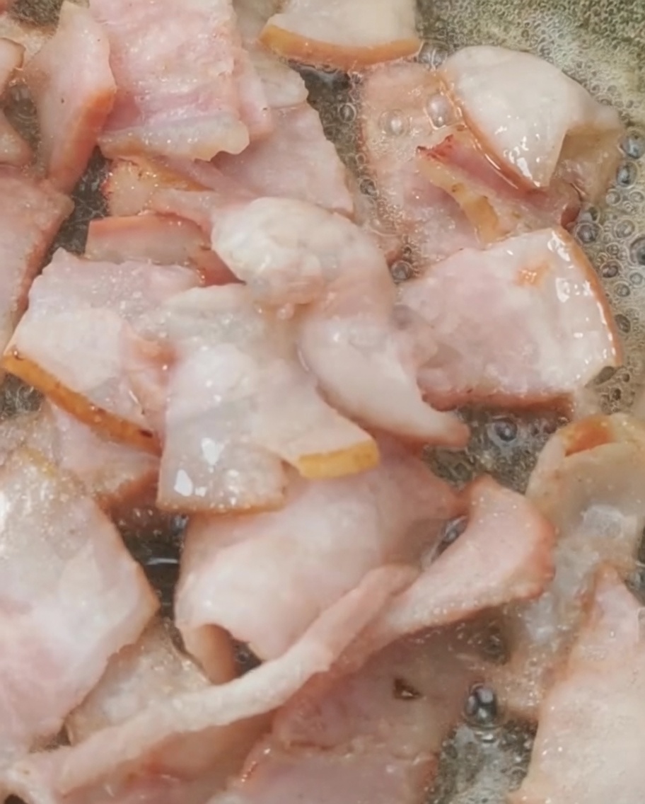 Freshly chopped cherry tomatoes being dropped into a pan containing golden browned bacon pieces.