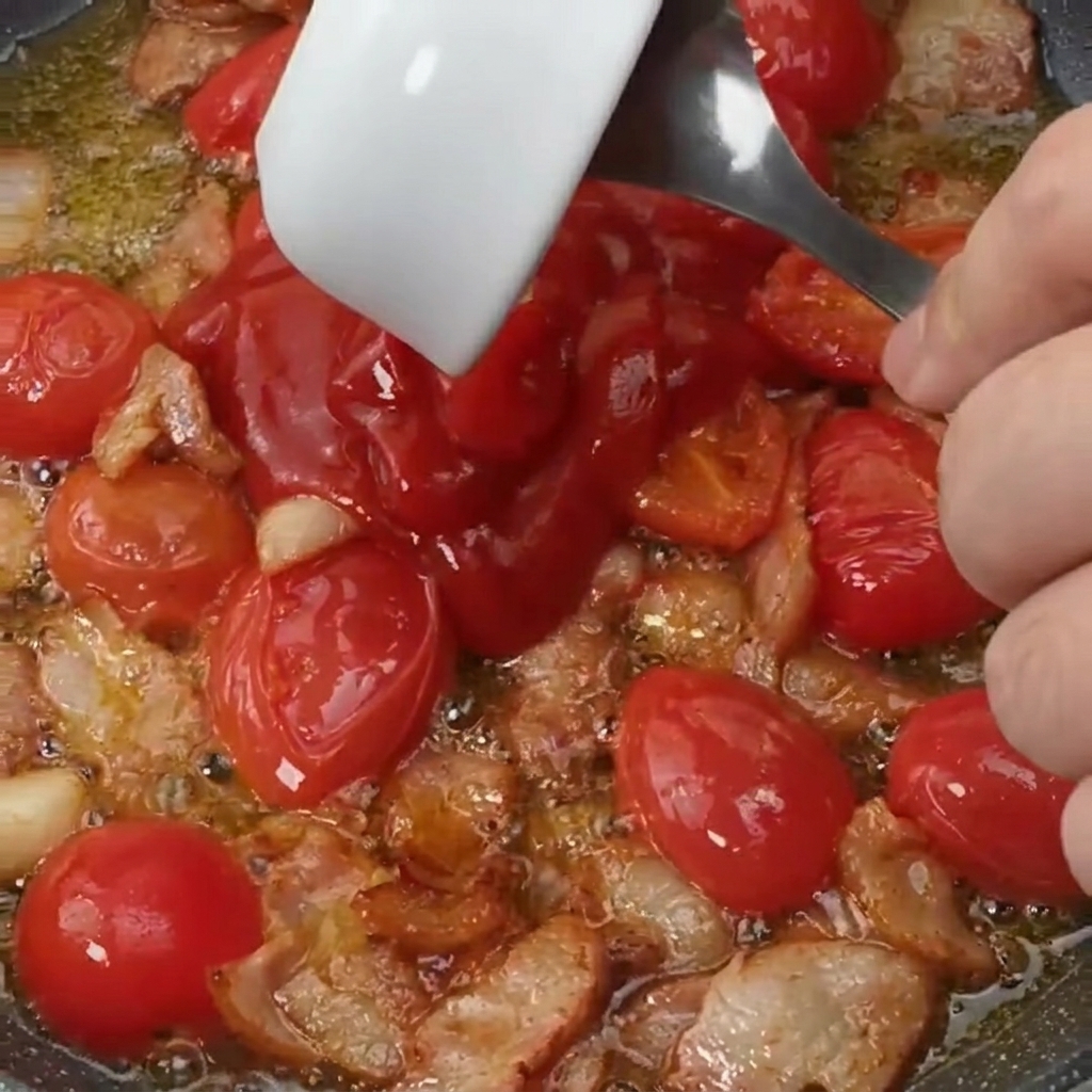 Tomato sauce and a sprinkle of sugar being poured into a pan with sautéed bacon and cherry tomatoes.