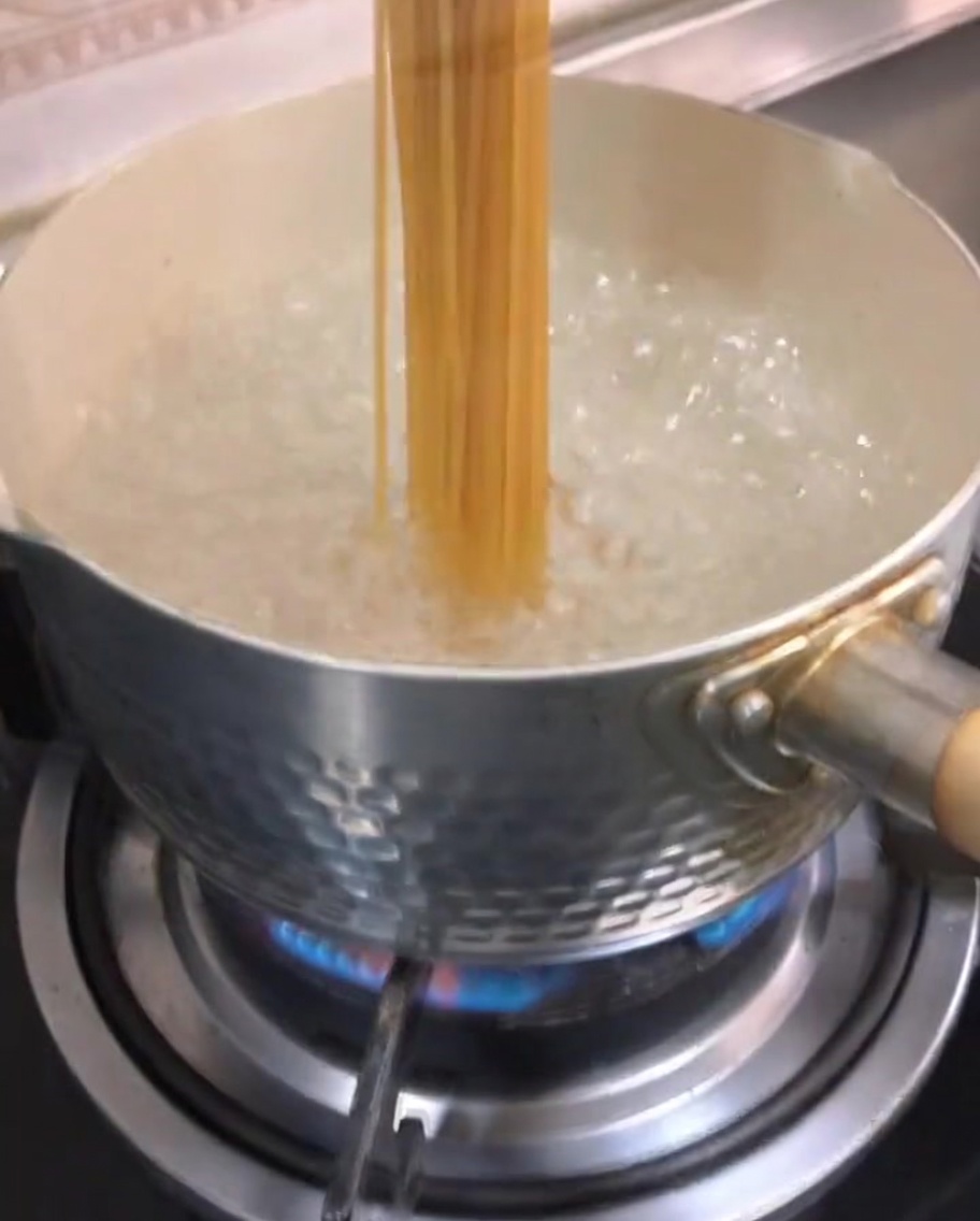 Dry spaghetti being submerged into boiling water in a pot.