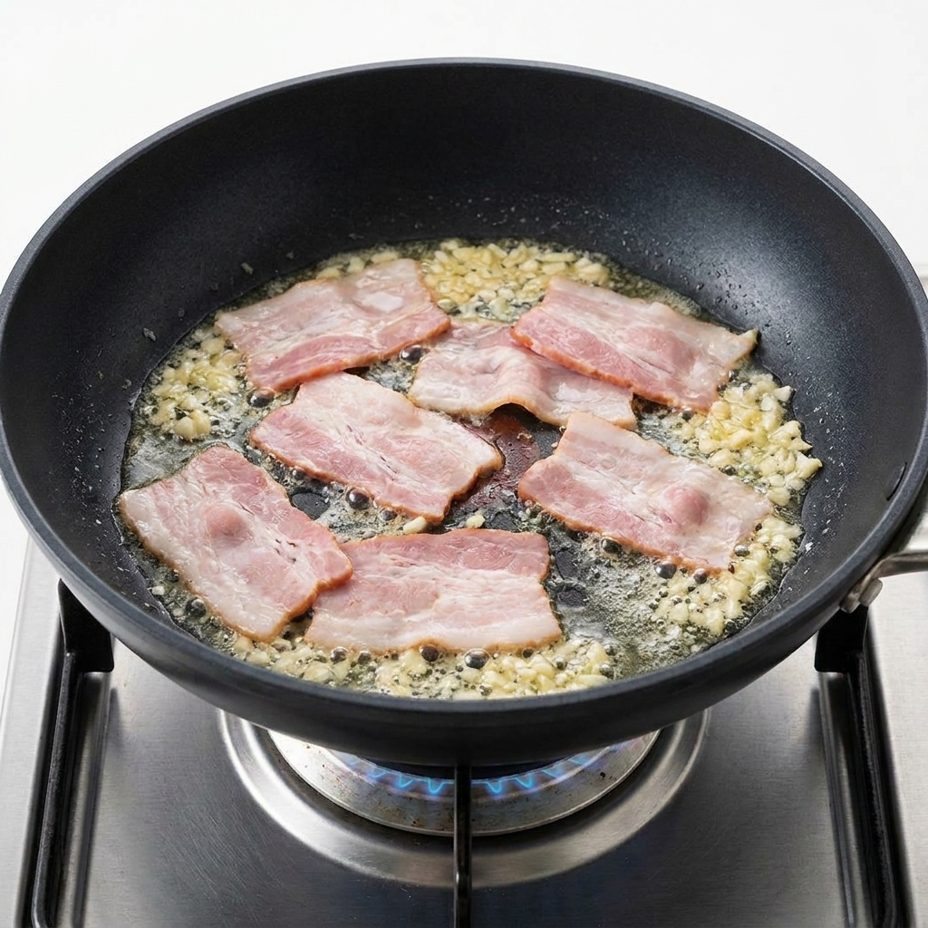 Bacon pieces sizzling in a pan alongside fragrant, golden minced garlic.