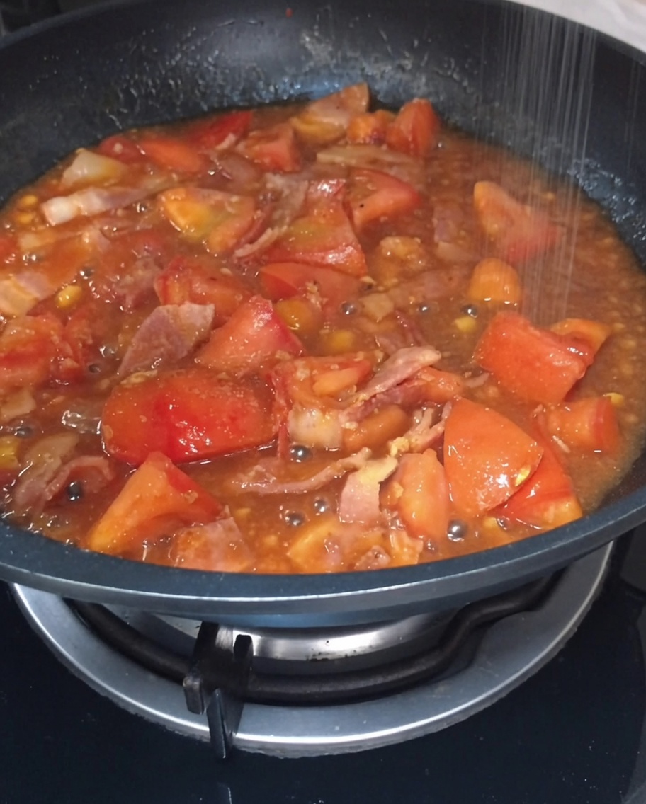 Salt and sugar being sprinkled into the bubbling tomato and bacon sauce in the pan.