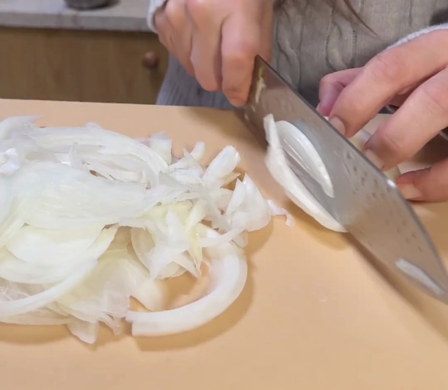 Thinly slicing a whole yellow onion on a cutting board.