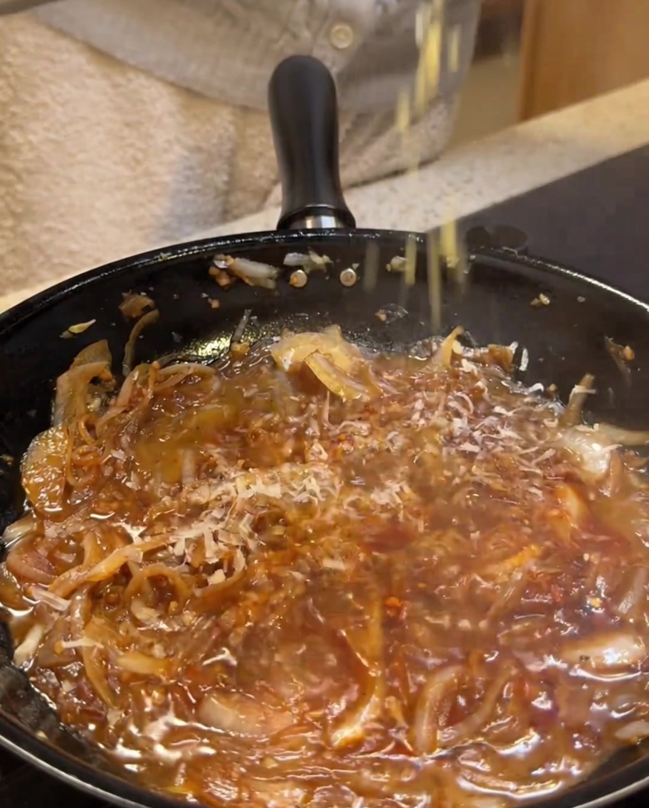 Parmesan cheese being grated into a creamy, simmering sauce base.