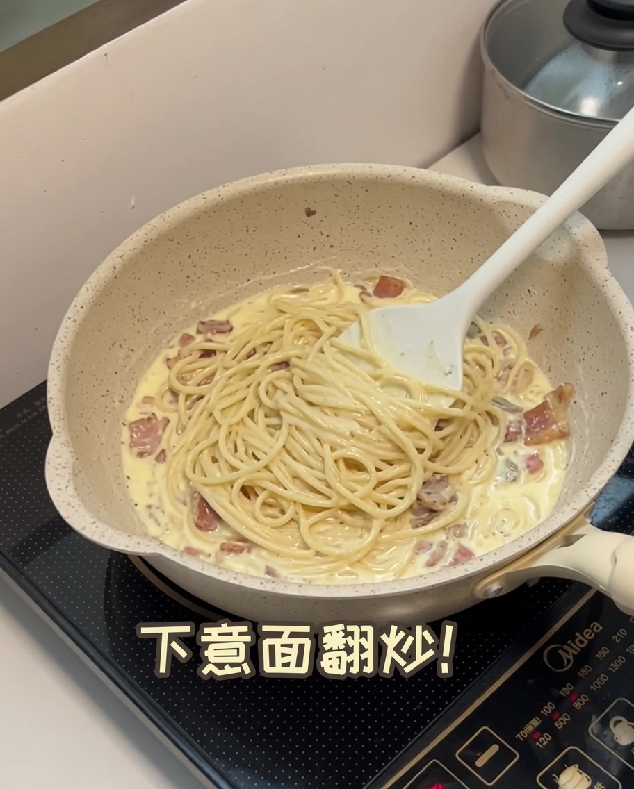 Cooked spaghetti being tossed into a creamy mushroom sauce in a pan.