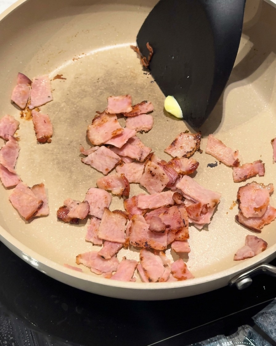 A knob of yellow butter melting into the pan alongside the browned bacon pieces.