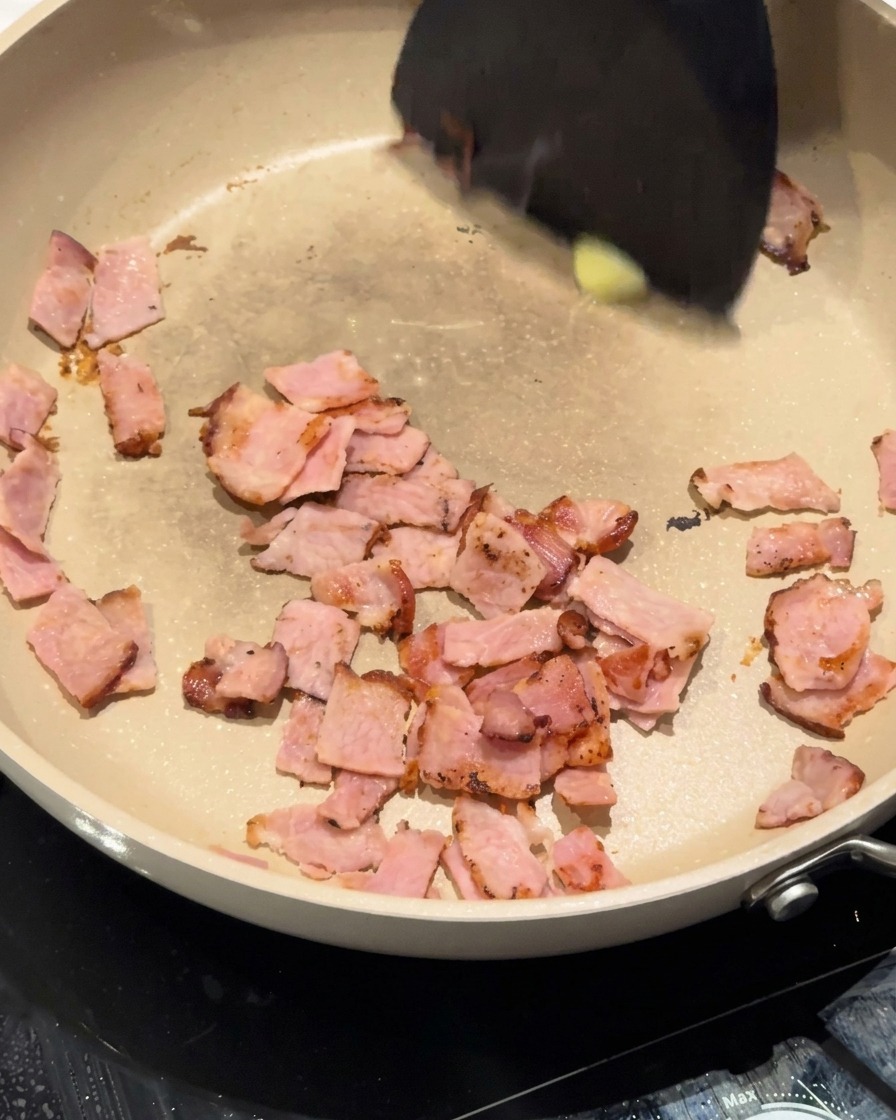 Chopped white onions being stirred in the pan with bacon and butter.