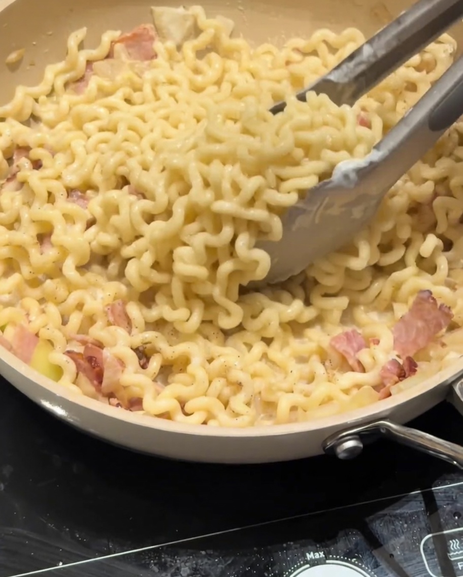 Parmesan cheese being sprinkled over a pan of creamy carbonara pasta.