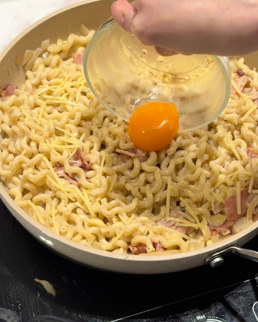 A fresh egg yolk being carefully placed into the center of a creamy pasta dish.