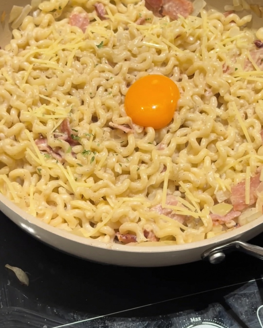 Dried parsley being sprinkled over the egg yolk and creamy carbonara pasta as a final garnish.