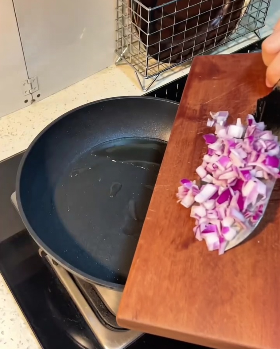 Diced bacon and onions sizzling in melted butter in a frying pan.