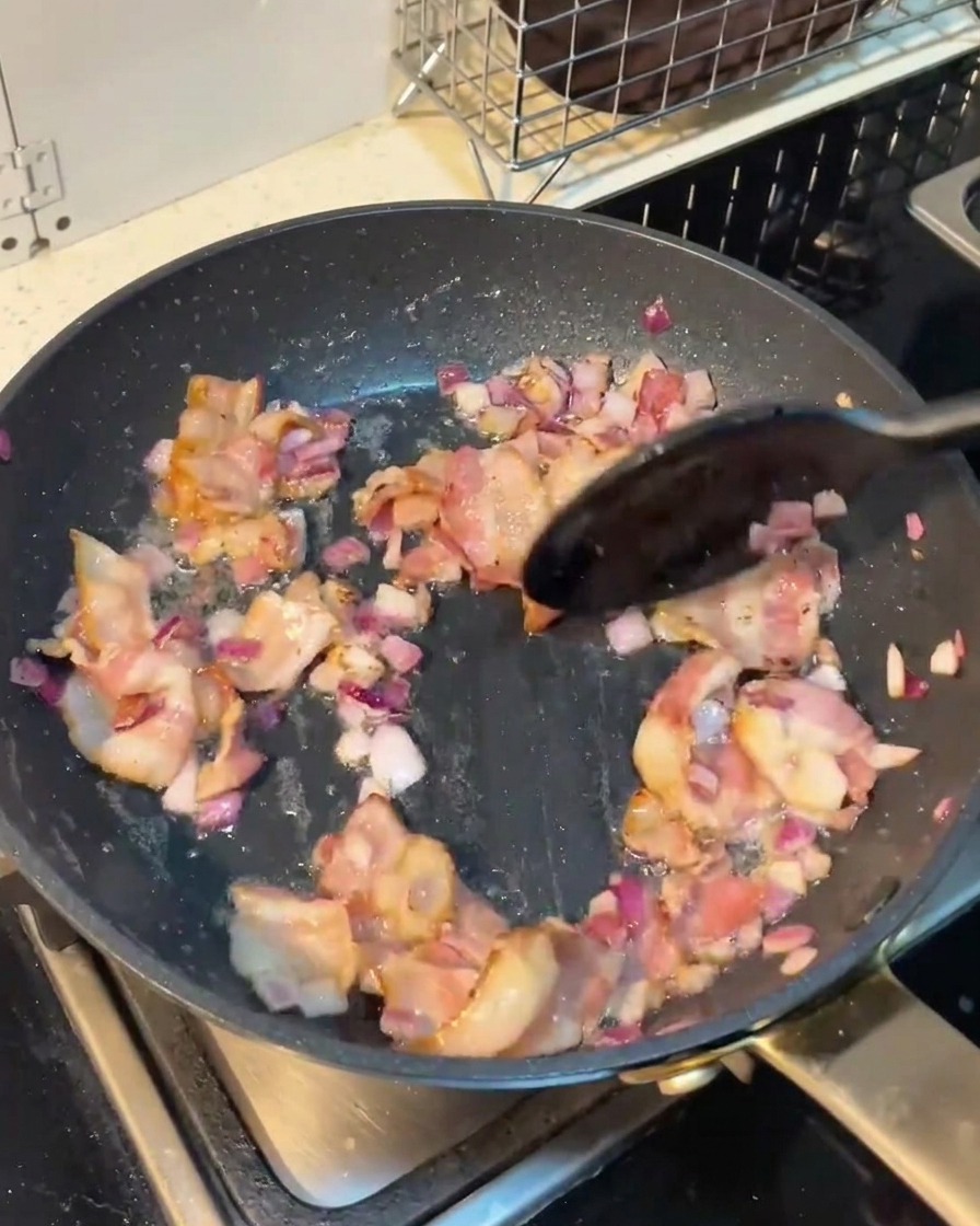 Sliced mushrooms being stirred into the pan with bacon and onions.