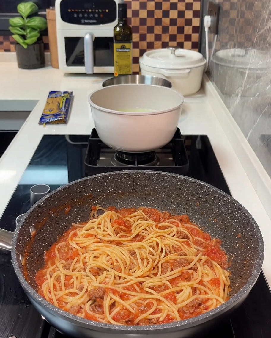 A pan filled with spaghetti and meat sauce with several slices of yellow cheese laid on top.