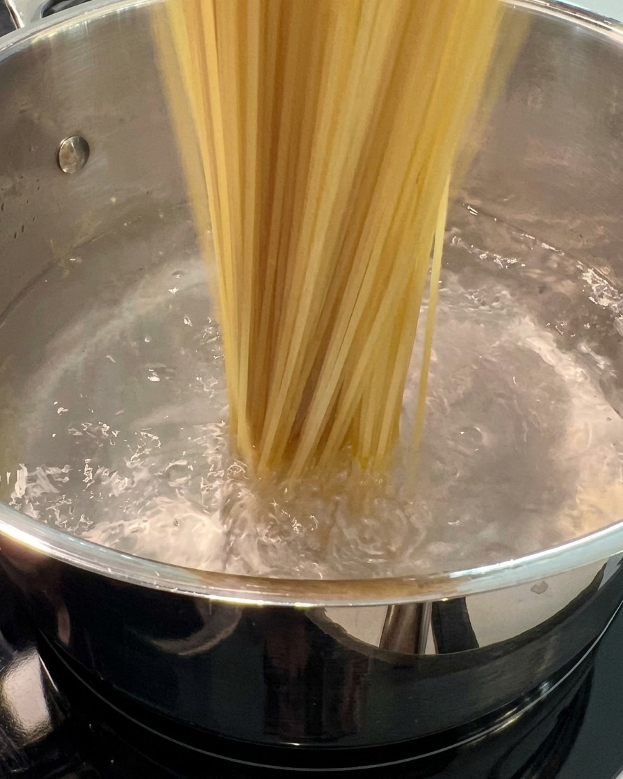 Dried spaghetti noodles being submerged into a large, boiling pot of water.
