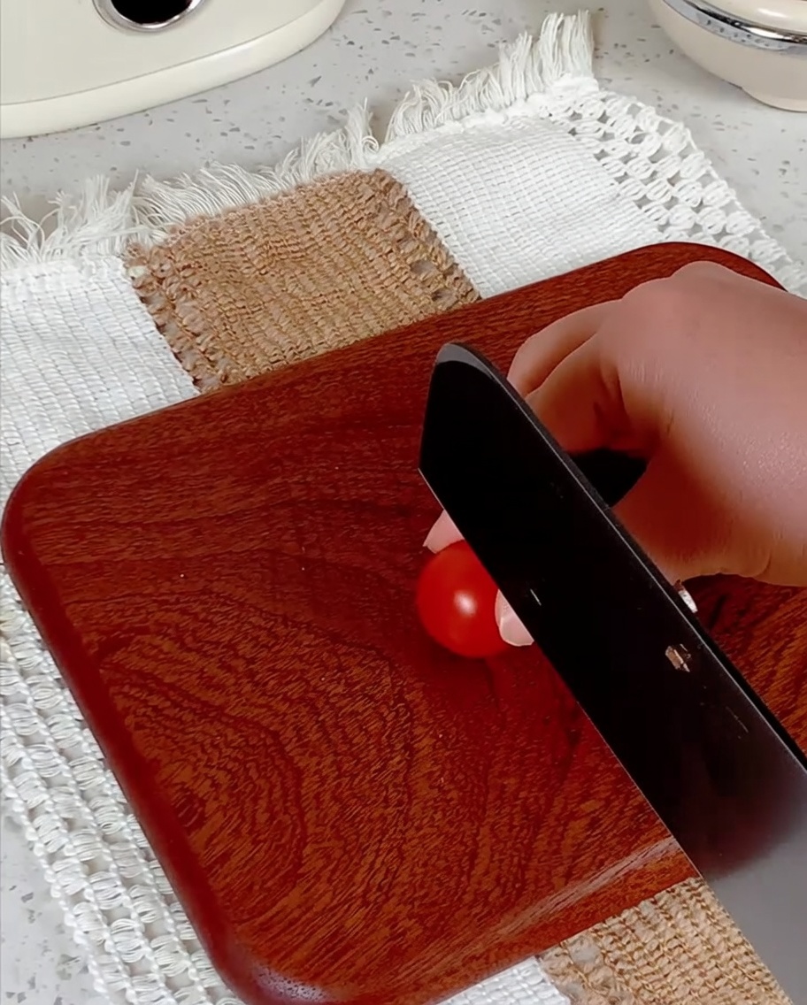 Cherry tomatoes being halved on a wooden cutting board with a knife.