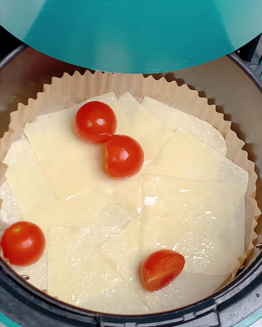 Cherry tomato halves scattered over oiled wonton wrappers inside an air fryer basket.