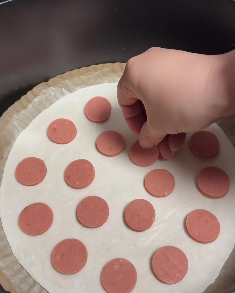 A scallion pancake topped with evenly distributed circular sausage slices.