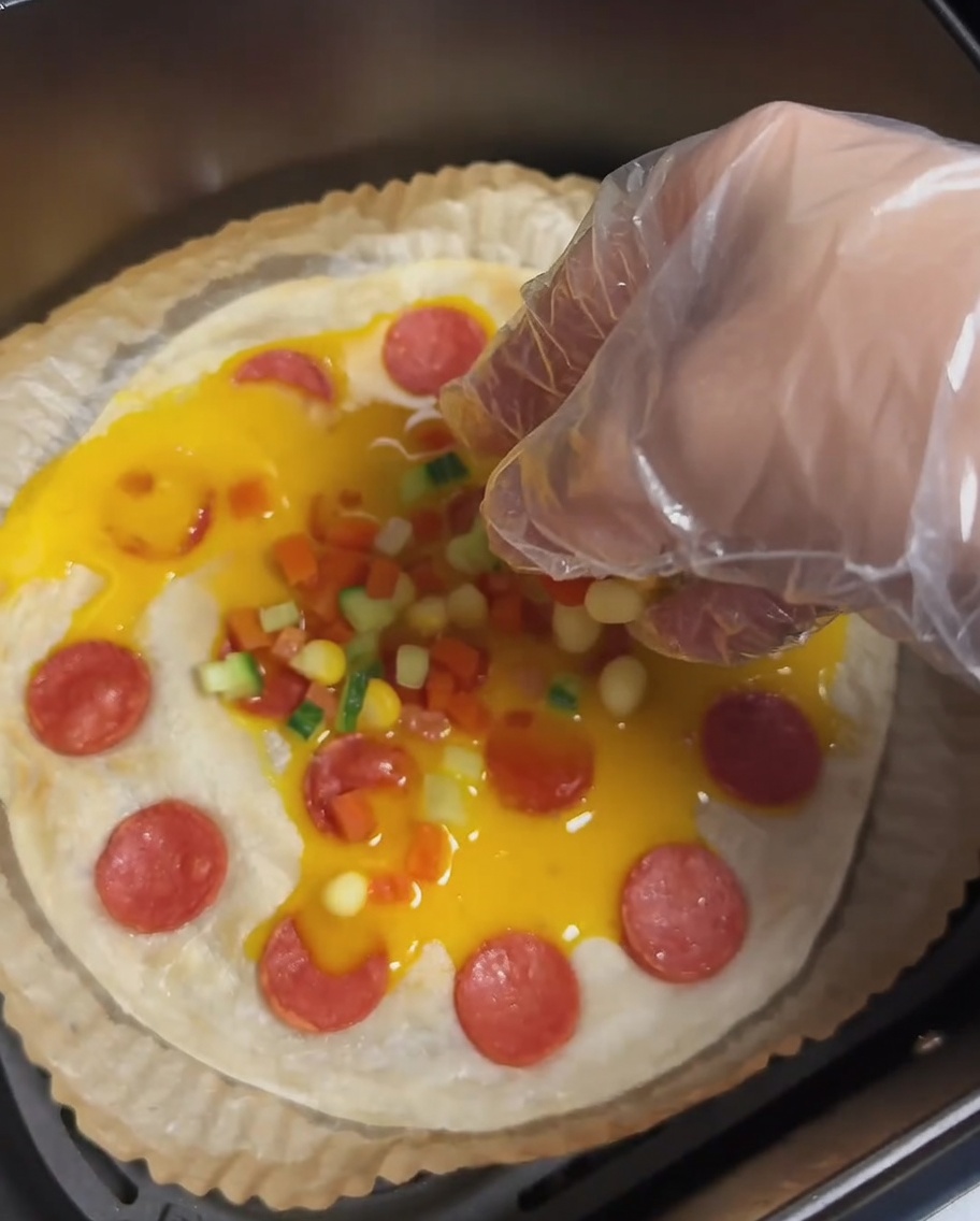 A scallion pancake with egg, sausage, and colorful chopped carrots, cucumbers, and corn kernels.